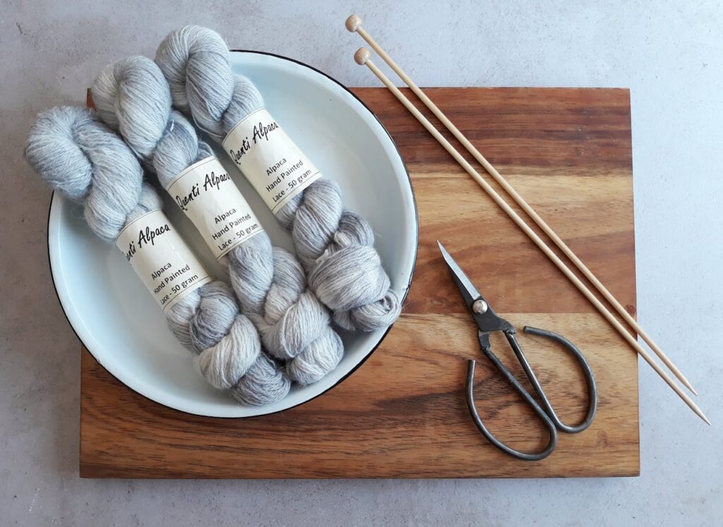 Hand-painted alpaca yarn with knitting needles and scissors on wooden board. Perfect craft scene.